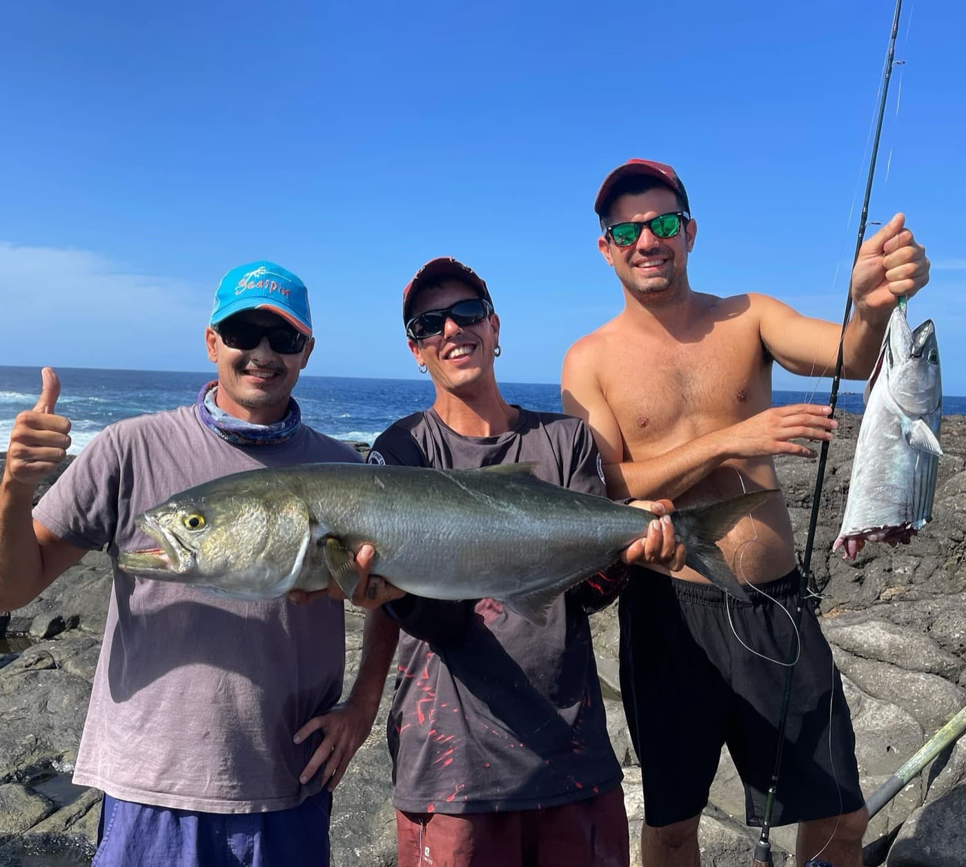 Three anglers on the volcanic shore with a large bluefish and a bonito