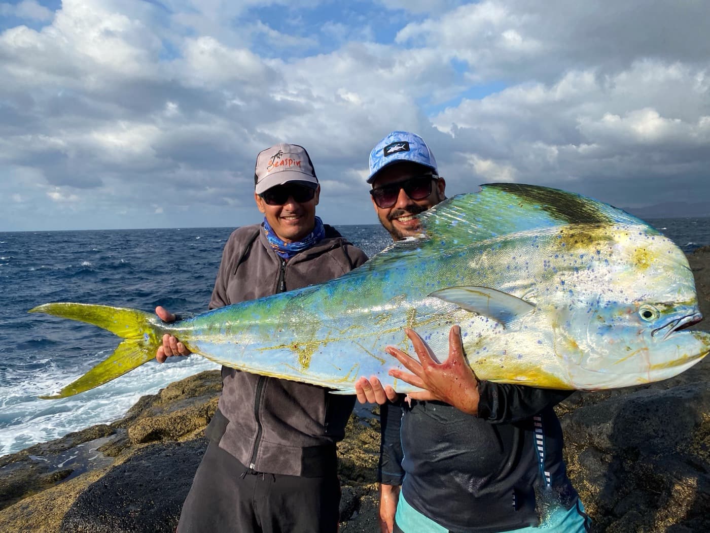 Local fisherman and guest on the volcanic shore of Lanzarote at sunset holding a dorado