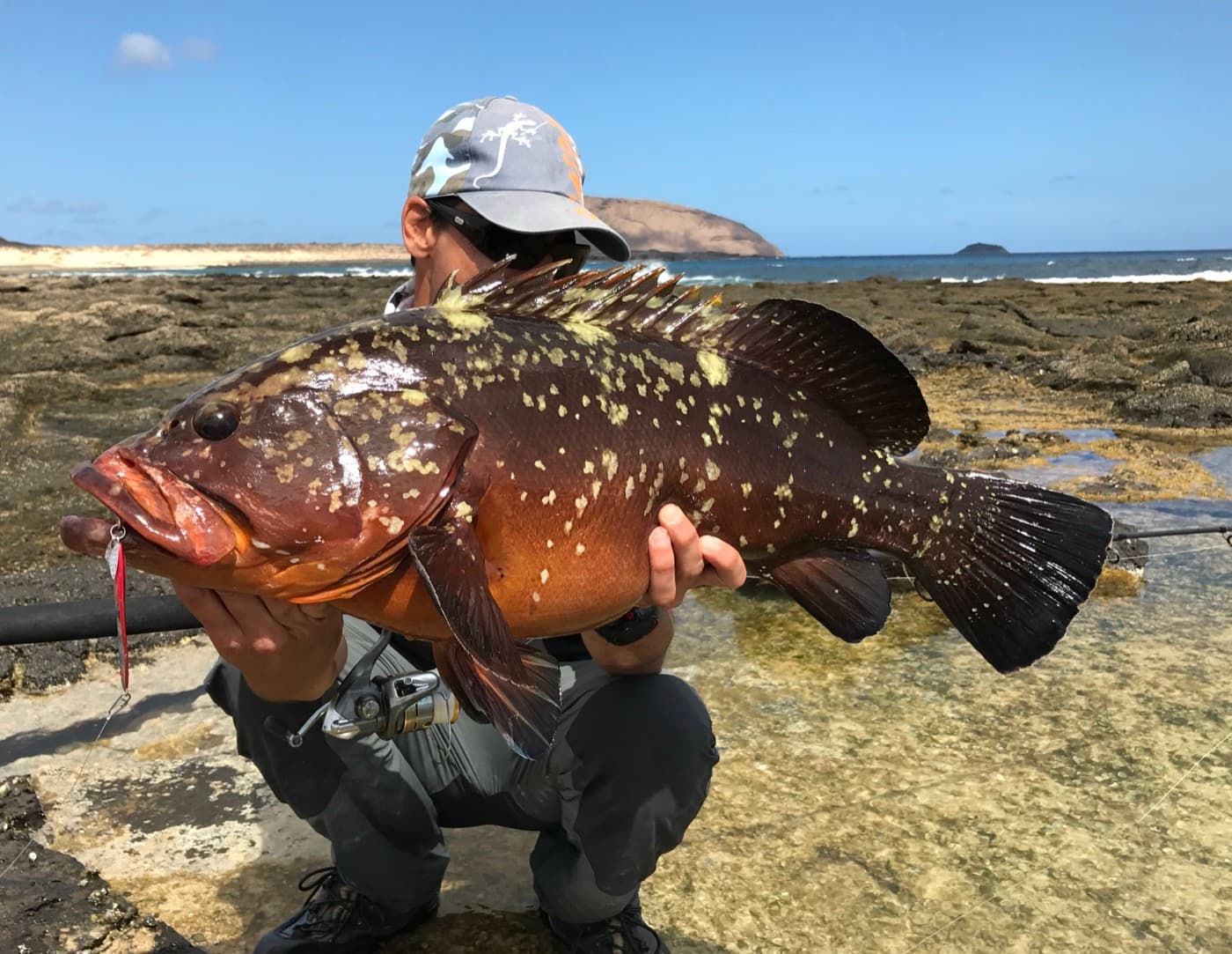 Local Lanzarote fishing guide holding a grouper caught from the rocks, with La Graciosa behind him
